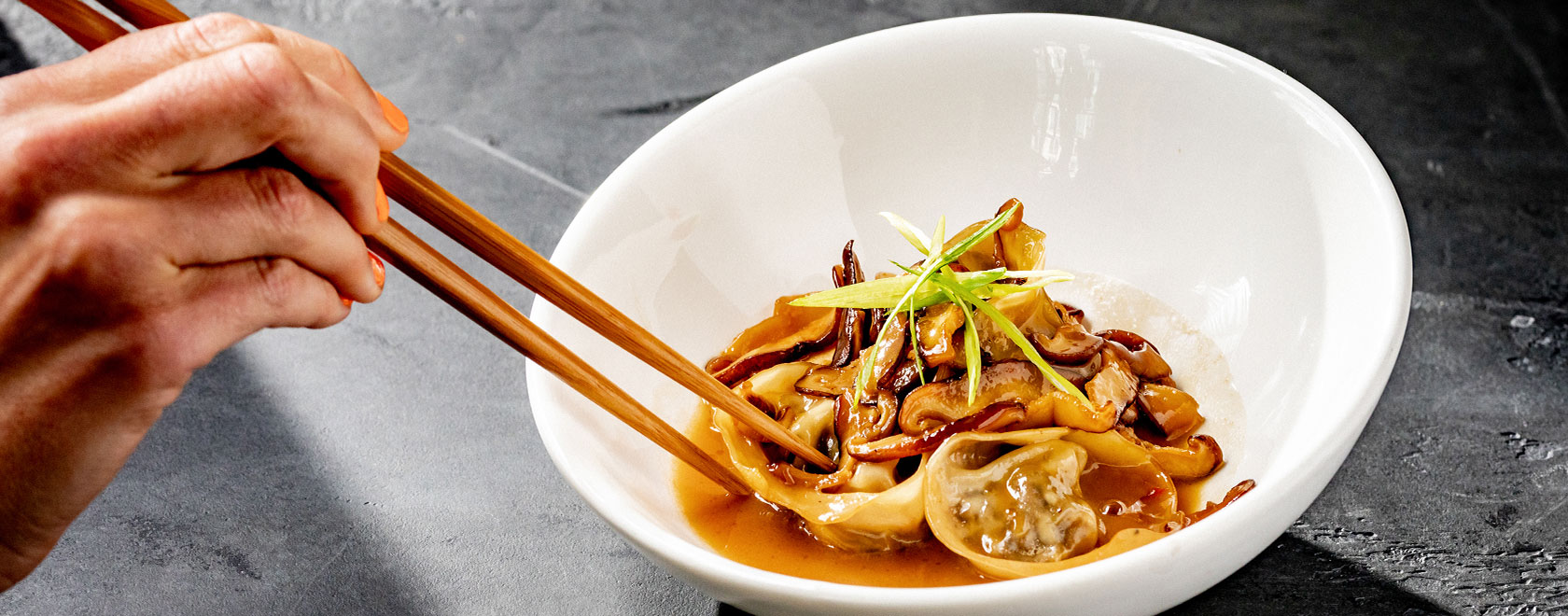 dumplings and garnish in a bowl with someone using chopsticks to hold a dumpling